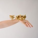 Closeup van arm en hand met daarop een handgemaakte gouden haarkrans voor bruiden gemaakt van metalen bloemen.