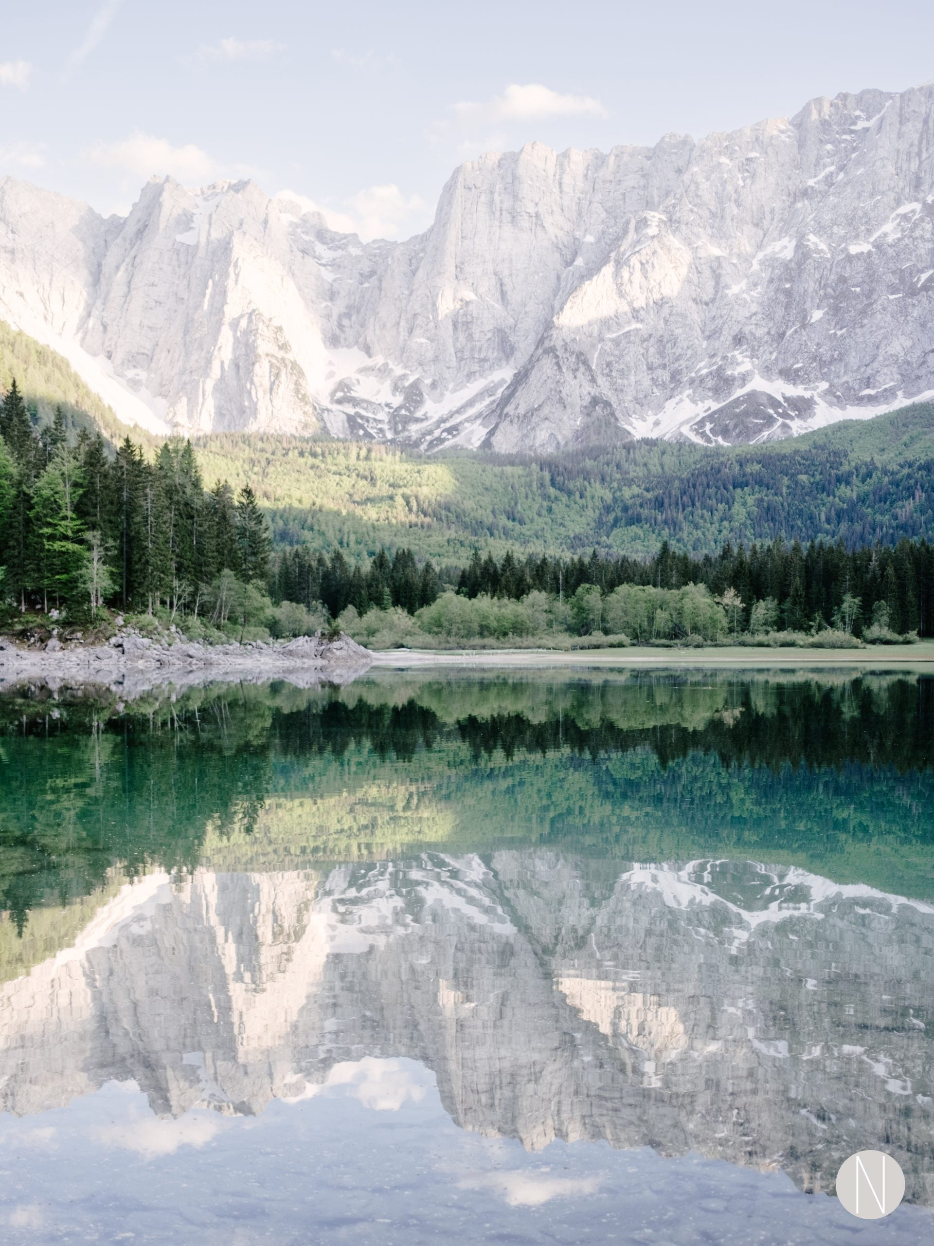 Secluded mountain lake surrounded by mountains and majestic trees, in pastel colours due to beautiful afternoon sunlight.