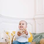 Branding fotografie kinderopvang Helden Opvang | Schattige kleine lachende jongen zitten op de grond in hoekje met heerlijke gekleurde kussen in Scandinavische sfeer spelend met houten autotjes bij Helden Opvang.
