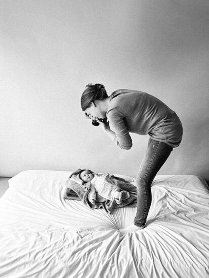 Zwart-wit foto van fotograaf die gebogen over een matras een baby fotografeert tijdens een rustige fotosessie.