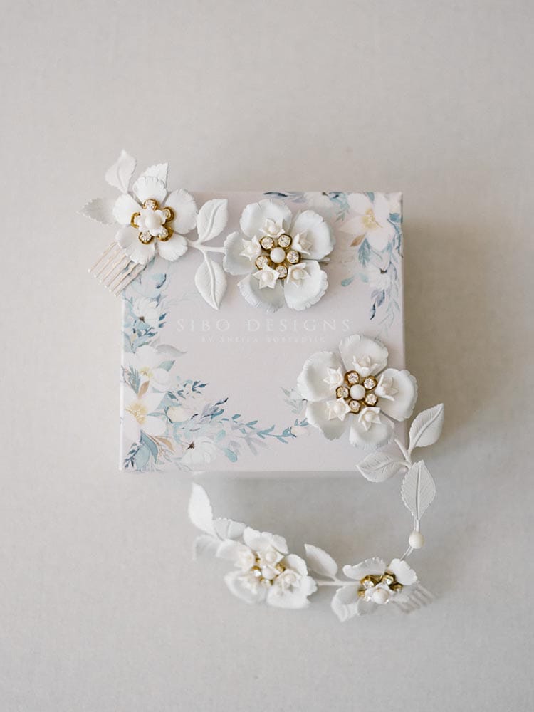 Minstens zo verfijnde witte bloemen haaraccessoires en een doosje van Sibo Designs op een lichte achtergrond.
